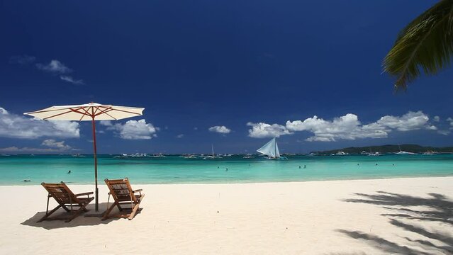 Sun umbrellas and beach chairs on tropical beach with palm trees. Summer vacation. Boracay