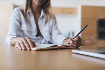 Crop woman writing in notebook in office