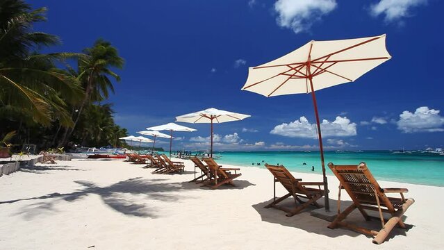 Sun umbrellas and beach chairs on tropical beach with palm trees. Summer vacation. Boracay