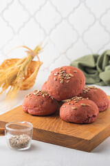 Rye and wheat flour bread buns with beetroot puree and sunflower seeds on a wooden board on a light concrete background. Baking bread with the addition of vegetable puree.