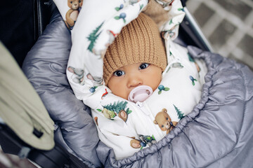 Dressed and wrapped infant lies down in baby carriage during walk in winter.