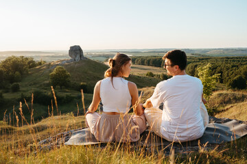 Man and Woman Practicing Yoga and Meditation Outdoors at Sunset with Scenic Landscape and Nature Miracle Giant Stone on the Background