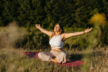 Young Woman Sunbathing and Meditating on the Mat Outdoors at Sunset with Beautiful Landscape on the Background