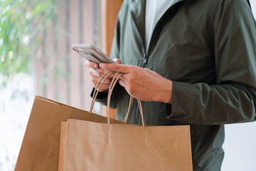 Close up of man`s hand holding smart phone research shopping  mall and shopping bags while walking on the street.