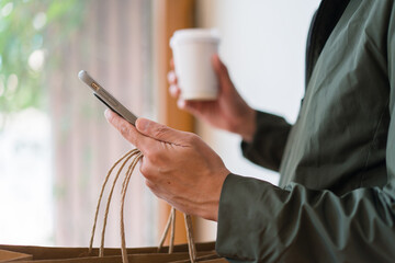 Close up of man`s hand holding smart phone research shopping  mall and shopping bags while walking on the street.