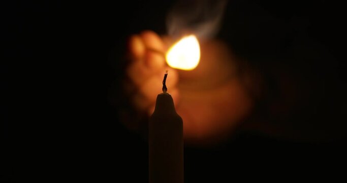 Hand lights candle using a match on black background