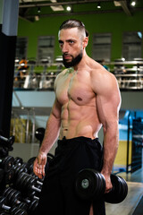 Fototapeta na wymiar A handsome muscular man with a beard is holding a dumbbell. Sports, healthy lifestyle