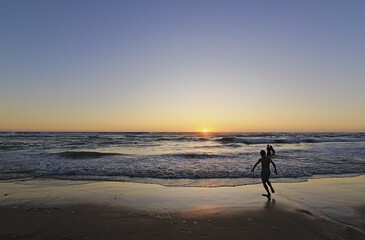 Fototapeta na wymiar niños corriendo hacia el mar en la puesta del sol