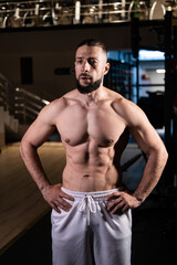 Fototapeta na wymiar A handsome muscular man with a spectacular body in white pants in the gym. Sports, healthy lifestyle