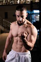 Fototapeta premium A handsome muscular man with a spectacular body in white pants clenched his hand into a fist. Sports, healthy lifestyle