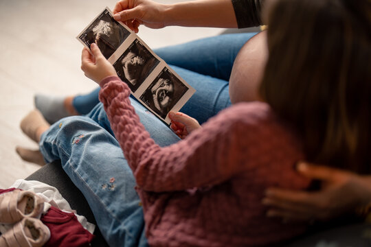 Shot of unrecognizable pregnant woman and her daughter looking at a sonogram picture at home.