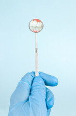 Professional Dentist tools in dental office - dentist mirror in doctor hand on blue background.