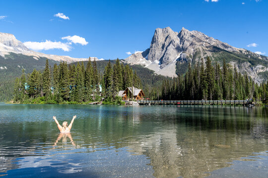 Blonde woman skinny dips in Emerald Lake, back facing camera with arms up, in Canada