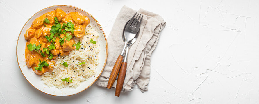 Traditional Indian dish chicken curry with basmati rice and fresh cilantro on rustic white plate on white concrete table background from above. Indian dinner meal, space for text