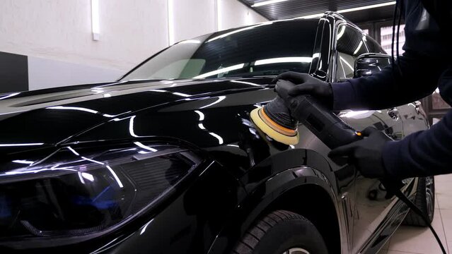 A man polishes a black car with a car polishing machine at a car dealership. Car detailing and polishing concept.