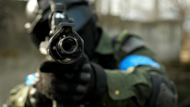 Close-up of a soldier in uniform with a blue armband and uniform, aiming a sniper rifle, rifle muzzle close-up. Military conflict. Airsoft.