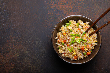 Authentic Chinese and Asian fried rice with egg and vegetables in ceramic brown bowl top view on dark rustic concrete table background. Traditional dish of China, space for text - 569998743