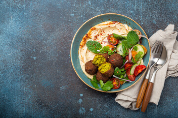 Middle Eastern Arab meal with fried falafel, hummus, vegetables salad with fresh green cilantro and mint leaves in ceramic bowl on stone rustic background top view. Arabic cuisine, space for text