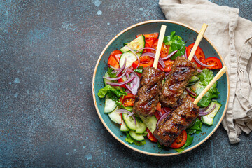 Grilled skewer meat beef kebabs on sticks served with fresh vegetables salad on plate on rustic concrete background from above. Traditional Middle Eastern and Turkish dish Kebab, space for text