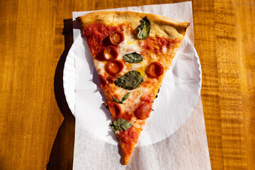 New York City Style Pepperoni Pizza Slice with Fresh Basil on a White Paper Plate