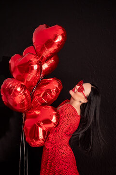 happy woman in a red dress holds a bunch of balls of hearts. Valentine's Day concept