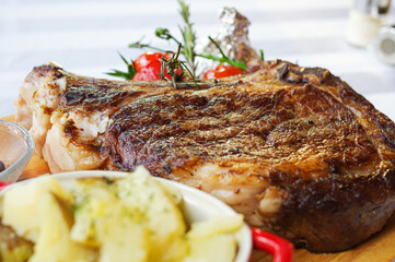 thick grilled bone-in steak rib-eye with tomato rosemary and mashed potato on wood tray