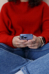 Young girl typing message on smart phone. Close up photo of unrecognizable female person sitting on couch and using mobile phone