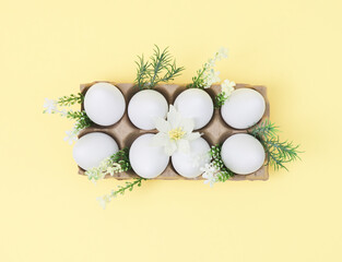 Decorative cardboard packaging with white Easter eggs and spring flowerson a yellow background,.