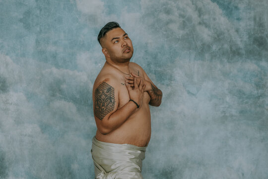 Filipino gay man standing looking up with hands on chest