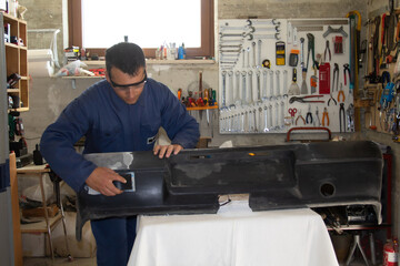 Image of an auto body repairer in his workshop repairing and polishing a car bumper
