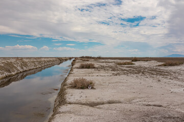 Fototapeta na wymiar Scenic view of the canals of Bonneville Salt Flats in Wendover, Western Utah, USA, America. Clouds appear as beautiful water reflection in the river. Barren salt desert landscape near Salt Lake City