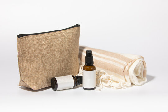 Mockup of a toiletry bag and amber colored glass bottles of cosmetic and facial and skincare products, accompanied by a rolled up sarong