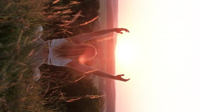 Back View on Woman Sitting in Meditation Yoga Pose and Catching Sun by Hands at Sunset Outdoors