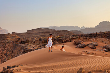 two girls playing on red dune sand in wadi rum desert at sunset