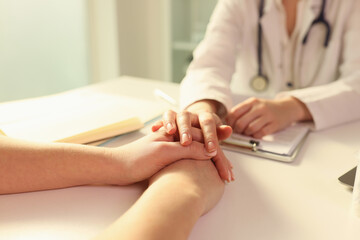 Female doctor puts her hand on hands of woman patient while explaining diagnosis.