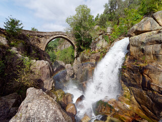 Fototapeta na wymiar Ponte da Misarela or Bridge of Mizarela in Montalegre, Portugal with a big waterfall next to it during a sunny day. Rural travel and holidays in nature. 