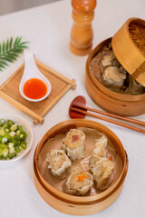 Fototapeta na wymiar Steamed four flavor dumpling dimsum in traditional bamboo steamer with sauce and green leek. Close up food photography