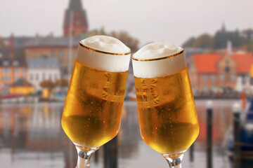 Pair of beer glasses making a toast with old German city blurred in background. Cold refreshing ale with white foam.