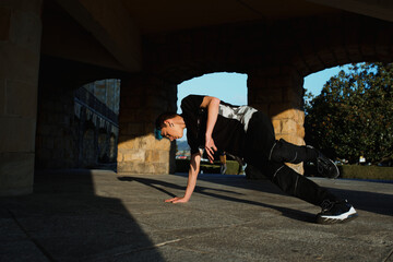 teenager boy with blue hair and sportswear dancing breakdace on the street. hip hop culture. street dancer doing pirouettes and stunts. © Alberto