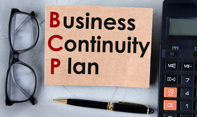 BUSINESS CONTINUITY PLAN - words on brown paper on the background of a calculator, glasses and a pen