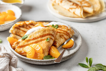 Crepes with fresh mandarin, caramel, cream in the filling and mint leaves on white textured background. Maslenitsa or Pancake week traditional concept