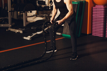 A young man with a beard does an exercise with battle ropes in the gym