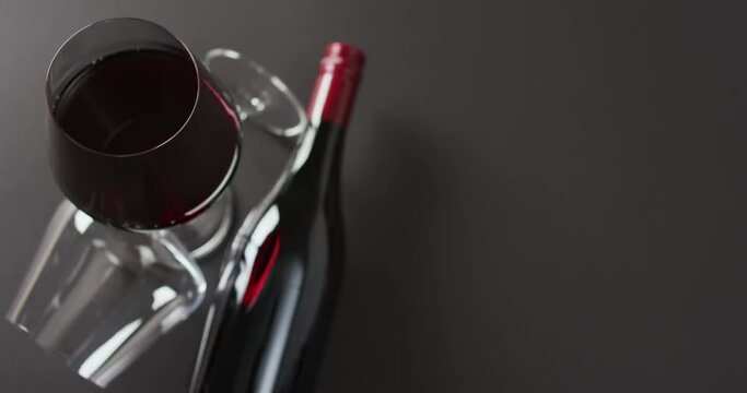Glass of red wine and red wine bottle lying on grey surface with copy space