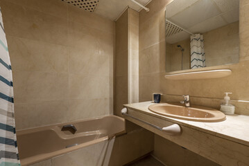 Conventional bathroom with marble countertop, brown porcelain bathtub with curtain, frameless mirror embedded in cream marble wall