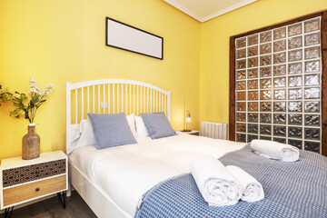 Double bedroom with white duvet and blue blanket, balcony with white doors and white four-section wardrobe