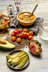 still life with tomatoes, pieces of tomatoes, lentils, a glass of water, kitchen towels, lentil stew and a plate of salad with tuna and tomatoes on a light wooden table