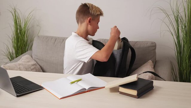 Homework finish. Teenager boy. Preparing school. Concentrated casual male kid putting work stuff into backpack sitting sofa light room interior.