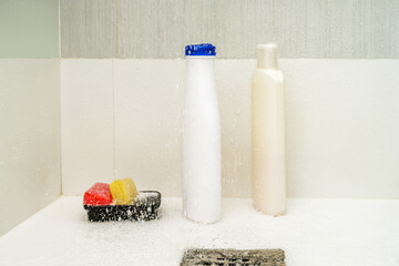 shower stall with a stainless steel drain with bottles of shampoo and soap bars splashed by the...