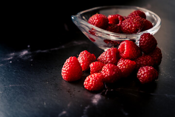 High view of a Serving of raspberries in a bowl on a black granite surface. Dark Food, horizontal orientation, space for text.