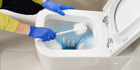 Wall mounted toilet cleaning with detergent. Woman hotel maid cleans a bathroom toilet with a scrub...